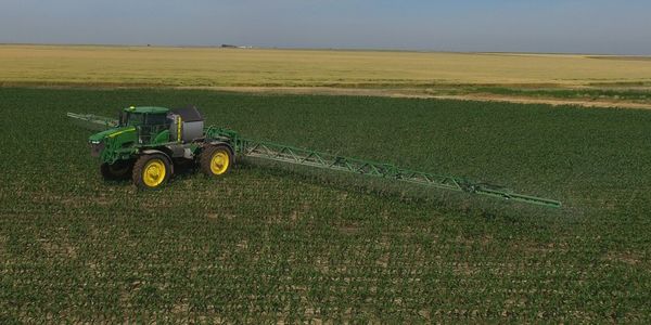 Aerial view of tractor spraying crops in green field